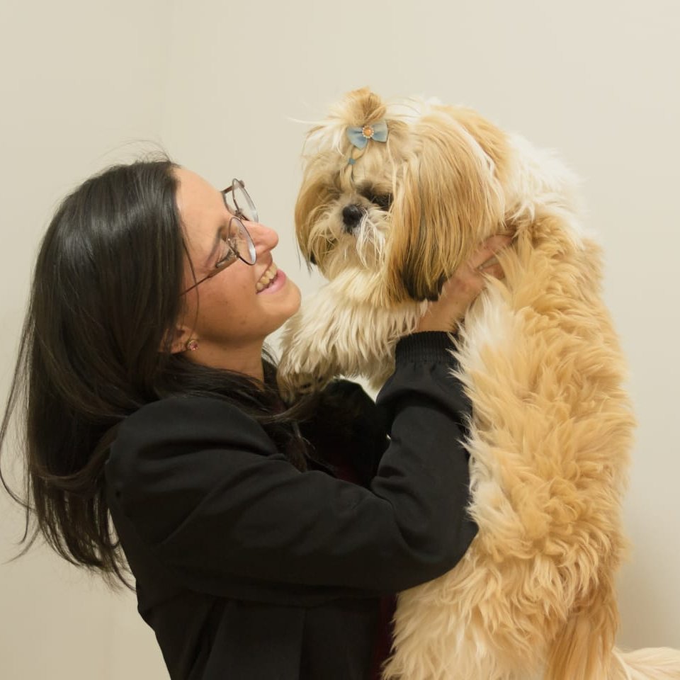 Dra. Mariana Duarte, hematologista veterinária em Uberlândia, sorrindo com um cão shih-tzu no colo